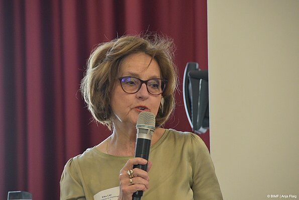 Foto MO VA: eine Frau mit Brille stehend mit einem Mikrofon in der Hand
