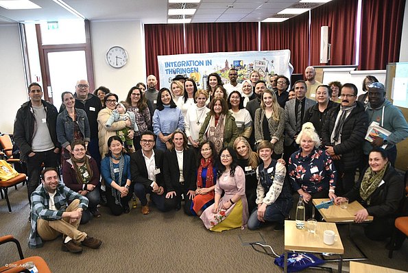 MO VA 20.04.2024 Gruppenbild viele Menschen, stehend und kniend vor dem Wimmelbild in einem Raum