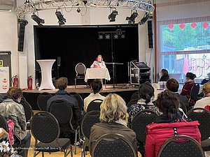 Menschen sitzend, eine Frau auf der Bühne