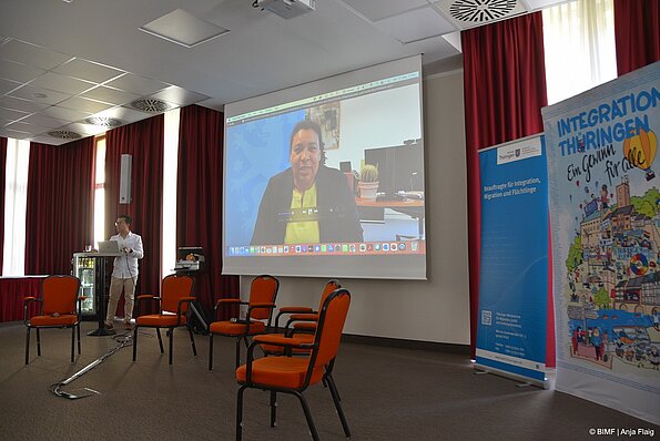 Foto MO VA: Online Grußwort Frau Ministerin Doreen Dennstädt, TMMJV, im Vordergrund Stühle, Rollup, Wimmelbild