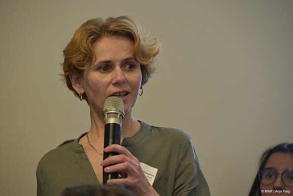 Foto MO VA: eine Frau stehend mit Mikrofon in der Hand, im Hintergrund eine weitere Frau sitzend