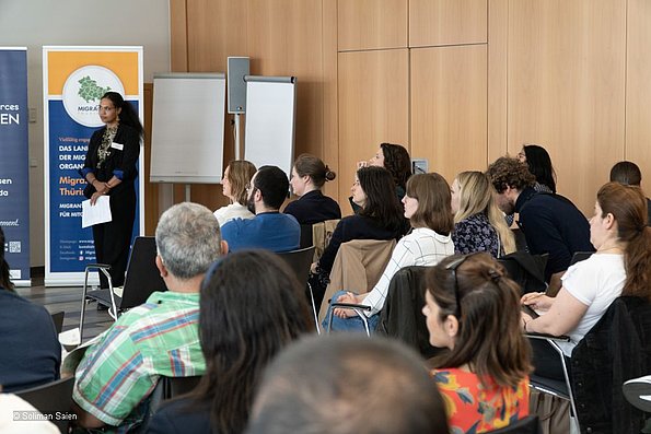 Veranstaltung politische Teilhabe 06.06.2024 - mehrere Personen sitzend, fotografiert von hinten, Dozentin vor Aufsteller stehend