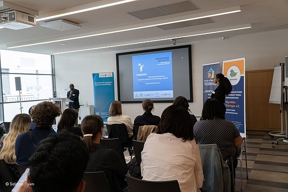 Veranstaltung politische Teilhabe 06.06.2024 - im Hintergrund 2 Dozenten vor Leinwand und Aufsteller, im Vordergrund Publikum sitzend