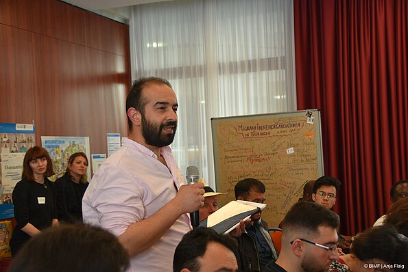 Foto MO VA: einige Menschen, ein Mann stehend mit Bart und Mikrofon in der Hand, in der anderen Hand Block