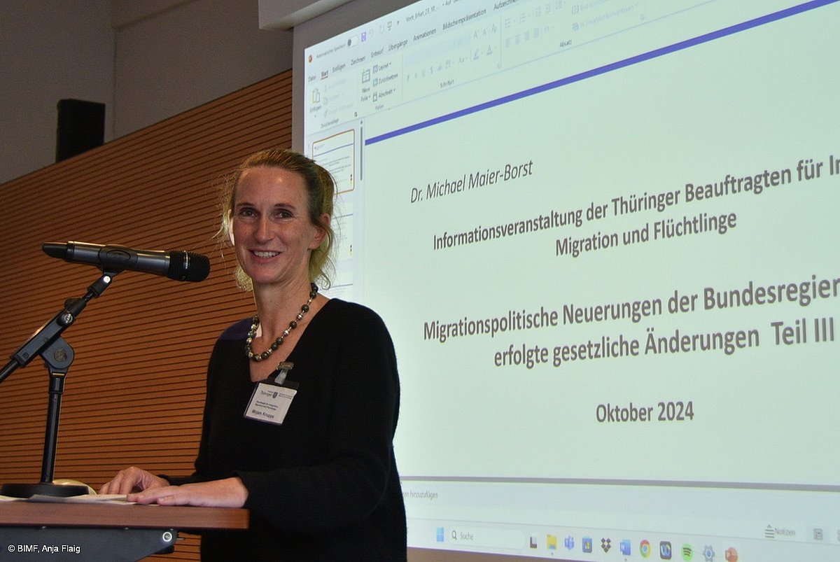 Thüringer Integrationsbeauftragte Mirjam Kruppa stehend am Mikrofon, im Hintergrund Präsentation von Dr. Maier-Borst