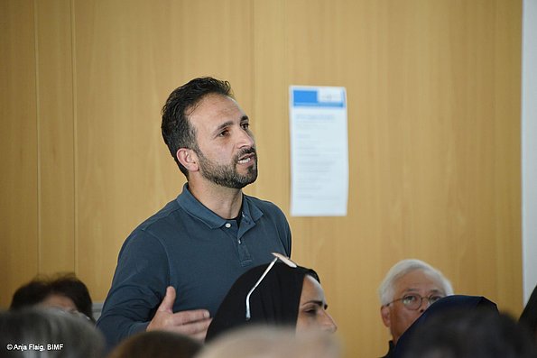 MO VA 17.05.2025 eine männliche Person stehend, mehrere Personen sitzend; Publikum