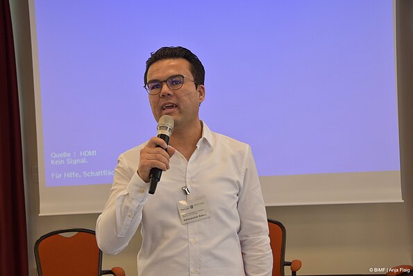 Foto MO VA: ein Mann mit Brille stehend mit Mikrofon in der Hand