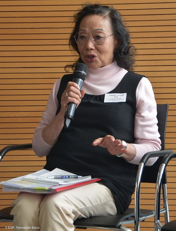 Veranstaltung Einbürgerung 2024-06-12 - eine Frau mit Brille sitzend auf einem Stuhl, sprechend in ein Mikrofon
