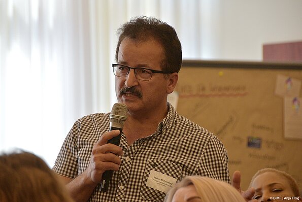 Foto MO VA: ein Mann mit Brille und kleinem Bart sprechend in ein Mikrofon