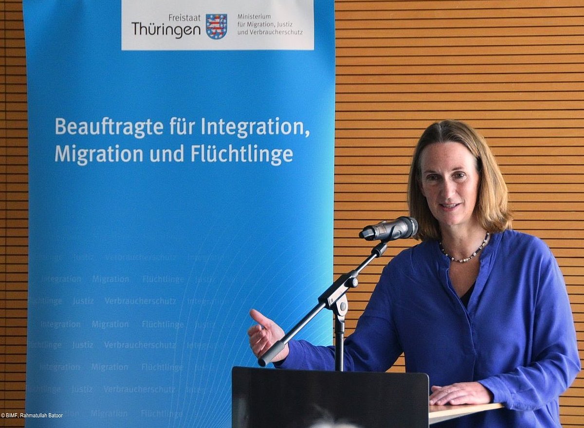 Veranstaltung Einbürgerung 2024-06-12 - Mirjam Kruppa, Beauftragte, stehend vor dem Mikrofon, im Hintergrund Rollup der Beauftragten