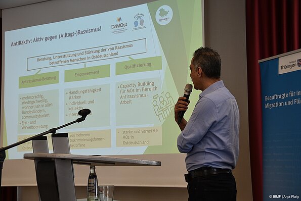 Foto MO VA: ein Mann mit Mikrofon in der Hand stehend mit dem Rücken vor einer Präsentation