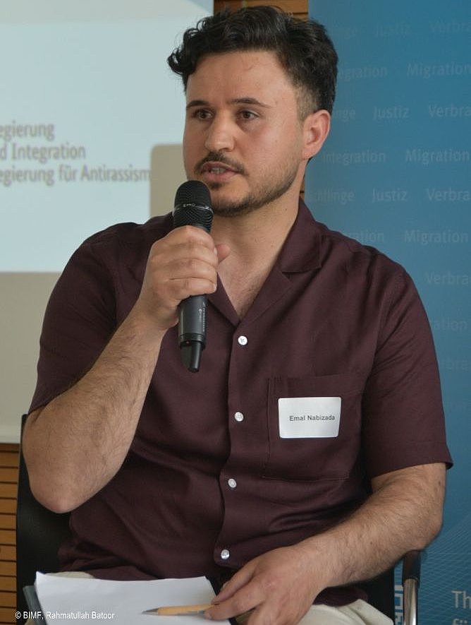 Veranstaltung Einbürgerung 2024-06-12 - ein Mann sitzend, sprechend in ein Mikrofon