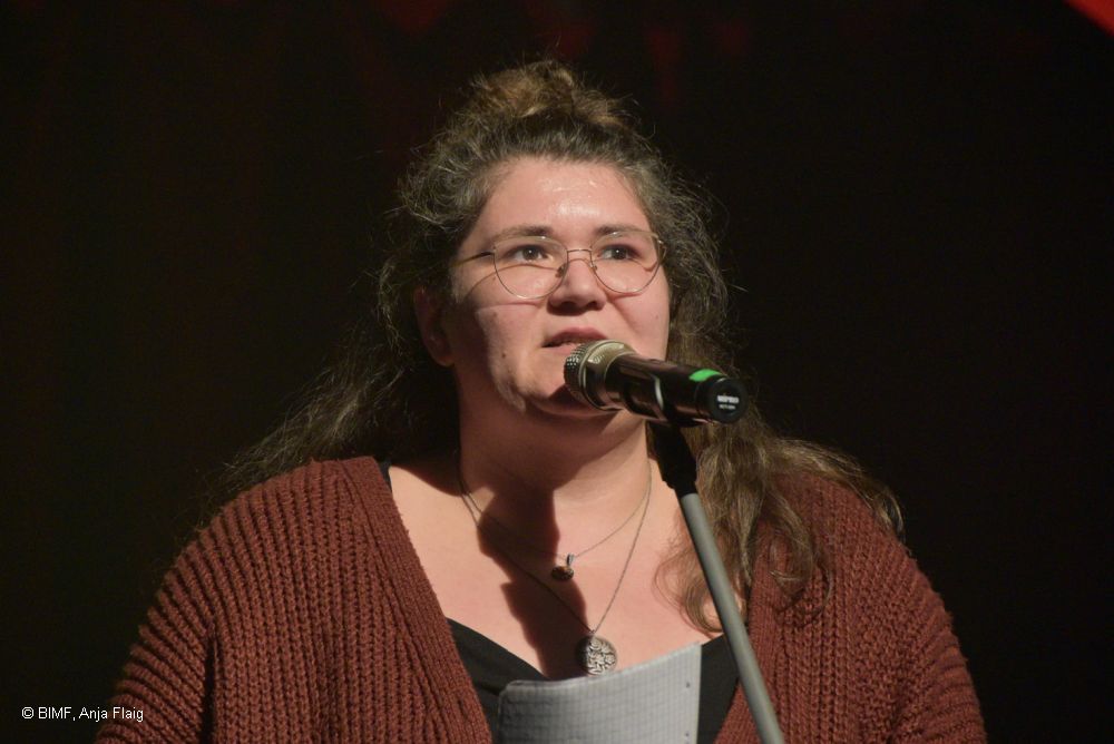 Frau mit Brille stehend vor einen Mikrofon