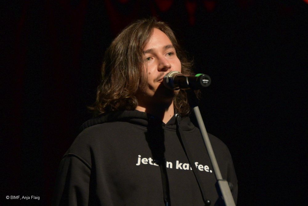 Mann stehend vor einem Mikrofon, schwarzer Hintergrund