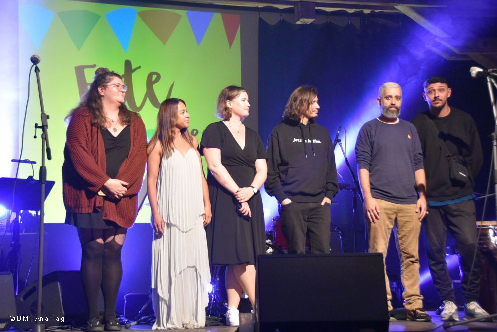 sechs Personen stehend auf einer Bühne, Poetry Slam