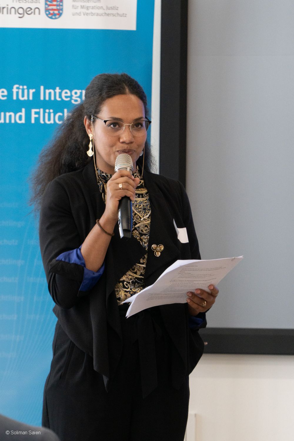 Veranstaltung politische Teilhabe 06.06.2024 - Frau stehend mit Zettel in der Hand und einem Mikrofon, Dozentin